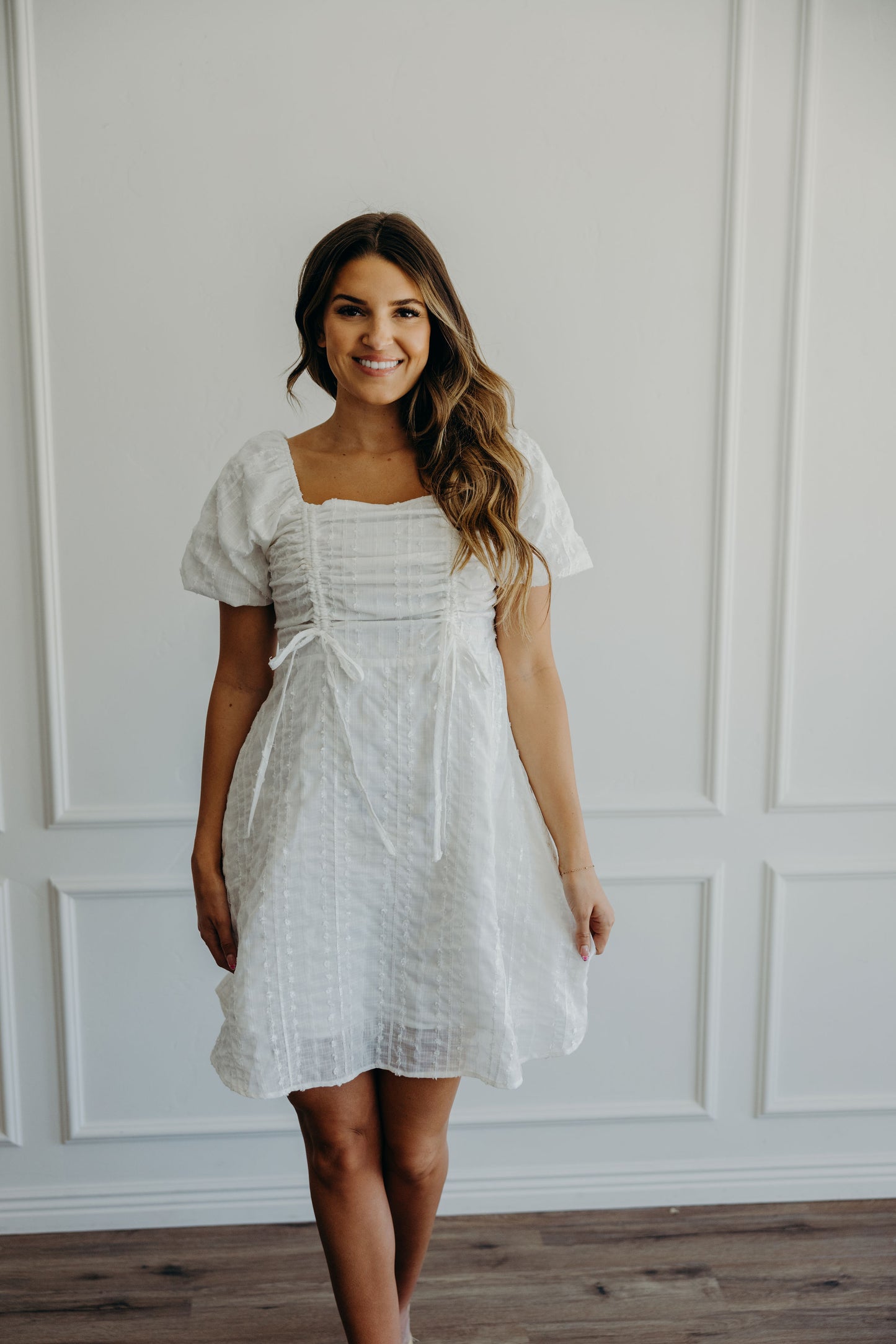 White fit and flare dress with textured detail, ruched and tie detail on bust with square neckline and short puff sleeves.