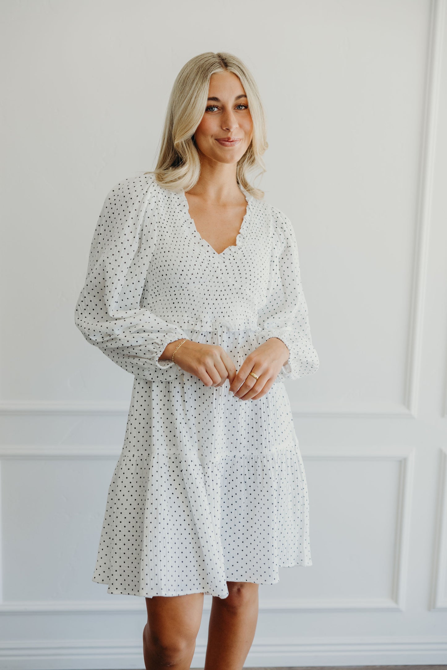White dress with black polka dot print with tiered skirt, natural waistline, v neckline, long sleeves and ruffle detail on waist and neckline.