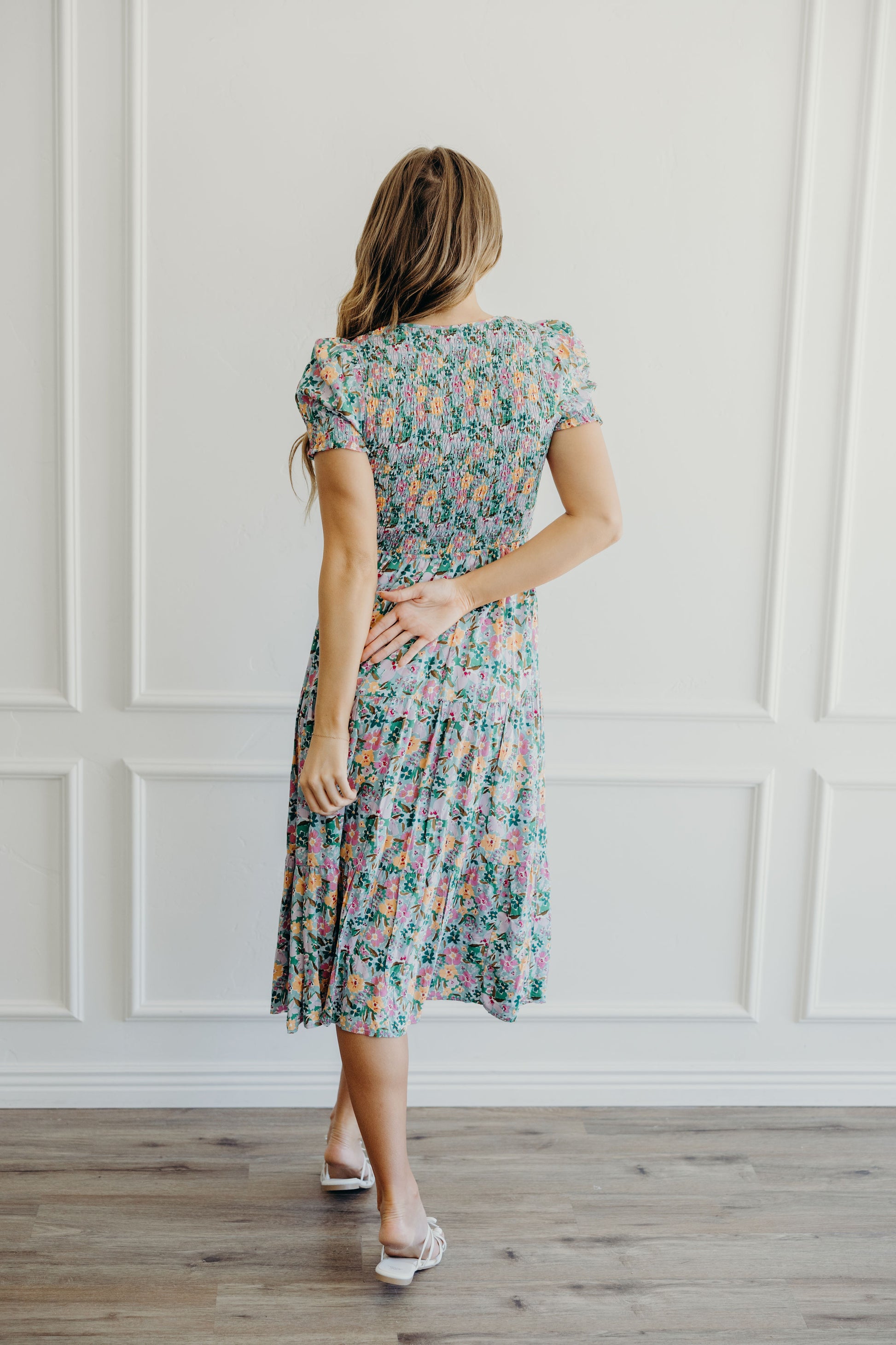 Back view of fit and flare green, yellow, and purple floral print dress with tiered skirt, smocked bodice, and short sleeves.
