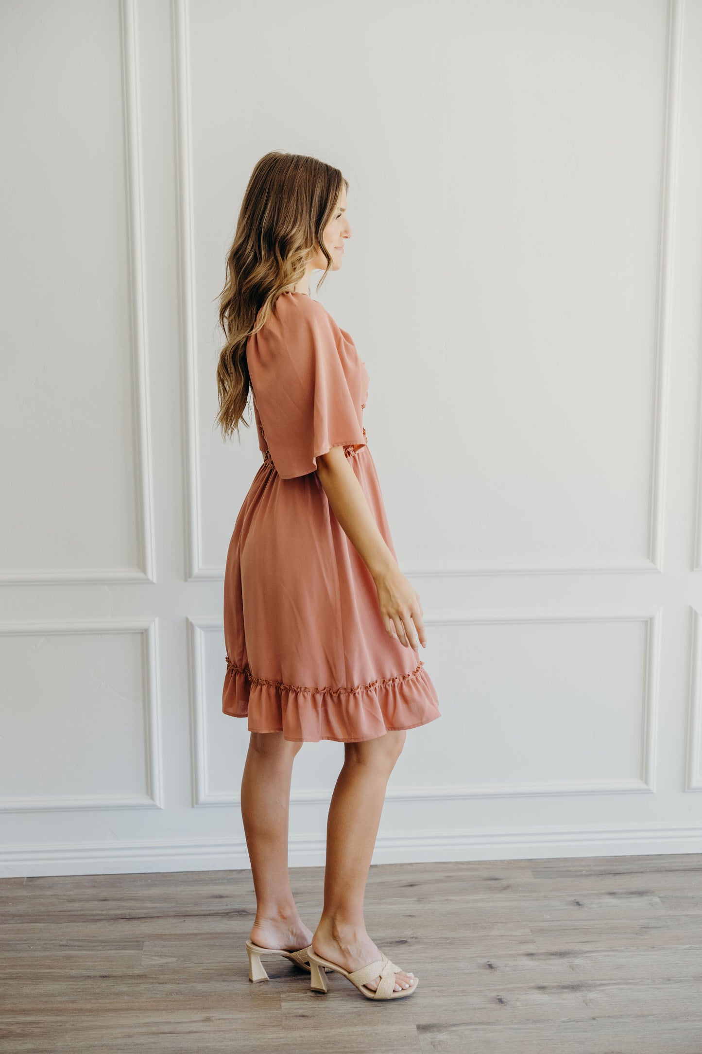Side view of pink knee length dress with ruffle hem and oversized flutter sleeves.