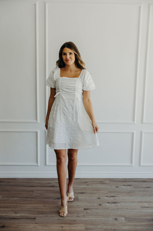 Short textured white dress with gathered tie detail on bust, short puff sleeves, and a line silhouette.