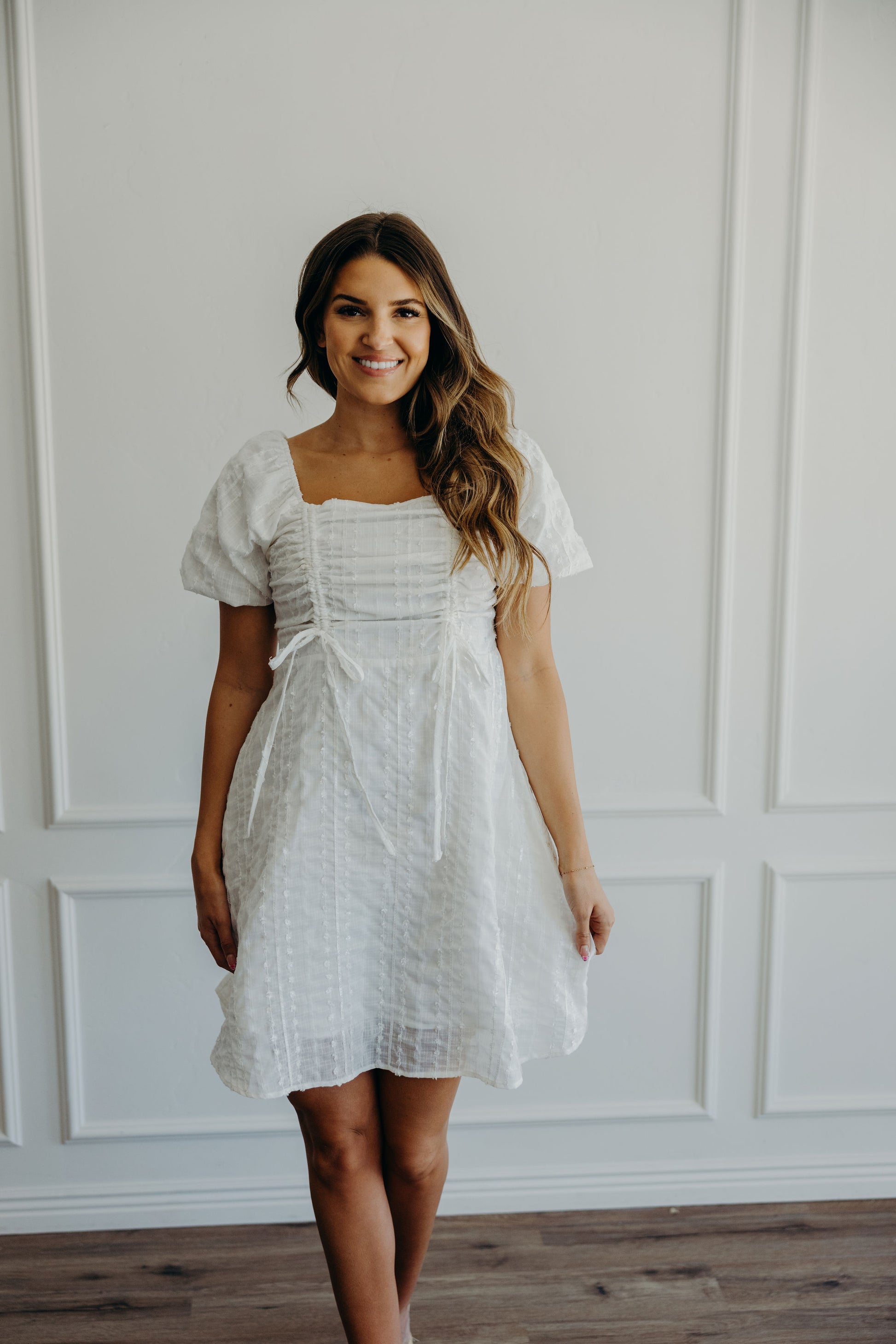 White fit and flare dress with textured detail, ruched and tie detail on bust with square neckline and short puff sleeves.