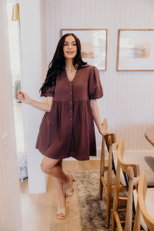 Knee length dark brown dress with buttons down the front and puff sleeves.